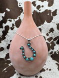 Load image into Gallery viewer, Turquoise and Silver Horseshoe Necklace on silver chain around a tan stand