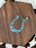 Load image into Gallery viewer, Turquoise and Silver Horseshoe pendant laying on wood block