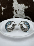 Load image into Gallery viewer, Blue Topaz and Sterling SIlver Earrings on white stand with cowhide background