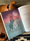 Load image into Gallery viewer, Book page with woman and horse and a saddle in the background
