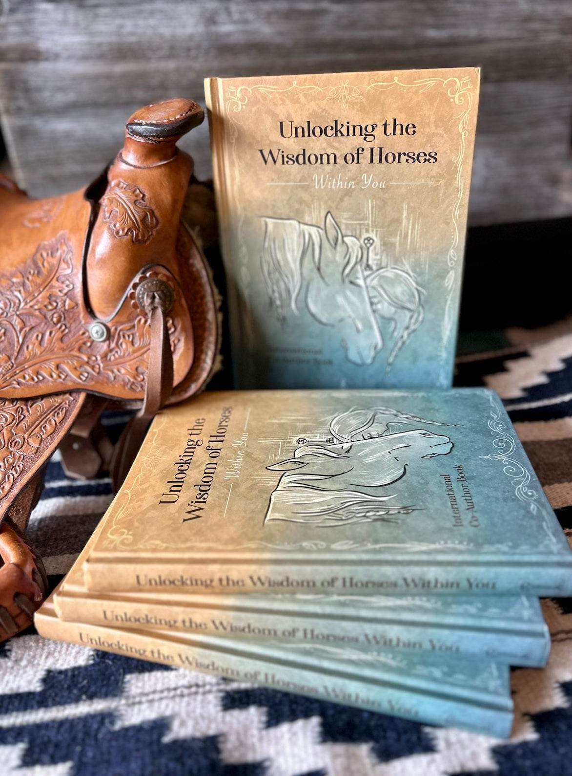 Western saddle with horse books next to it, wood background laying on blue and white blanket