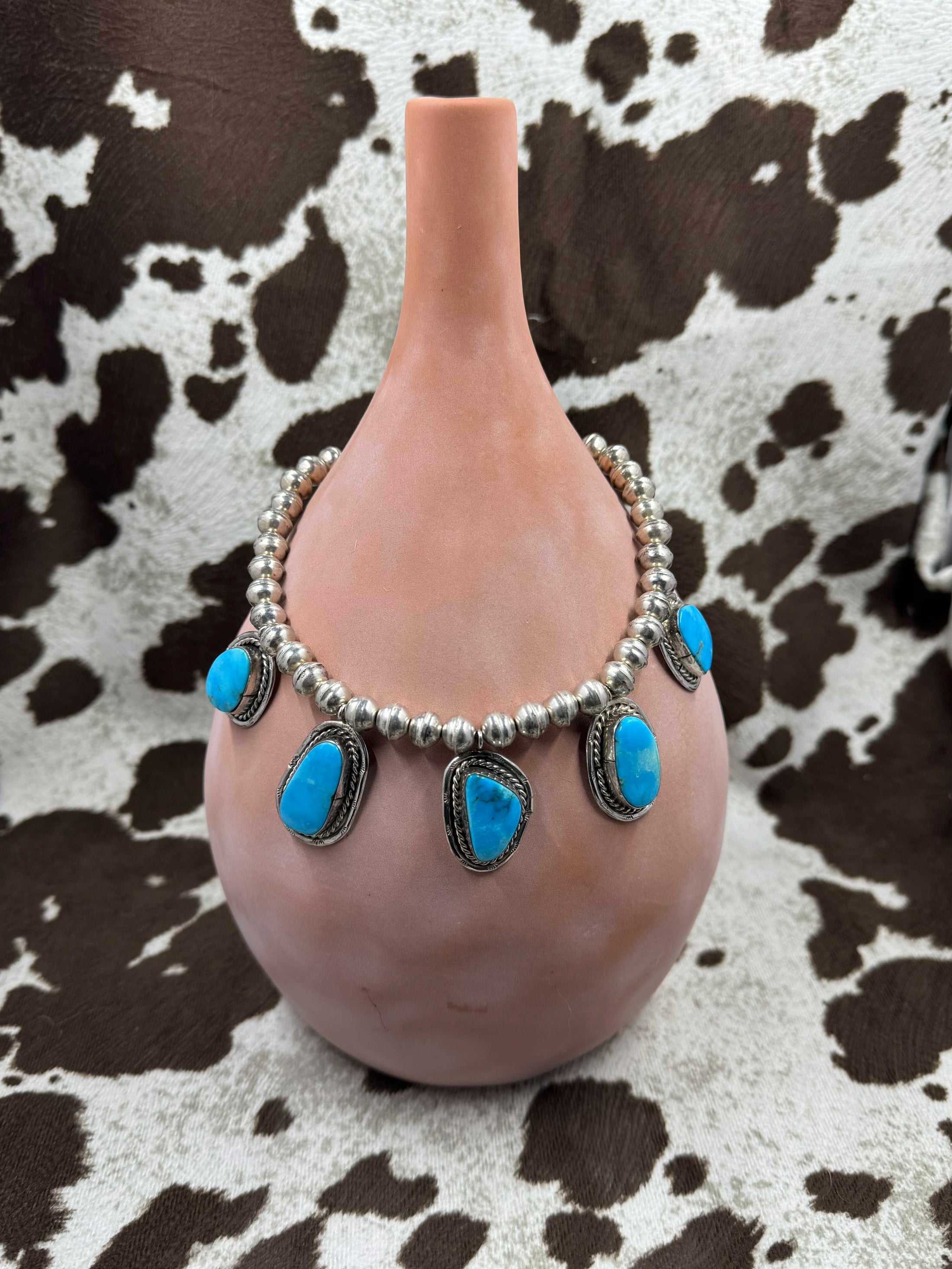 Vintage 5 Stone Silver and Turquoise Necklace hanging on brown bottle with cowhide background