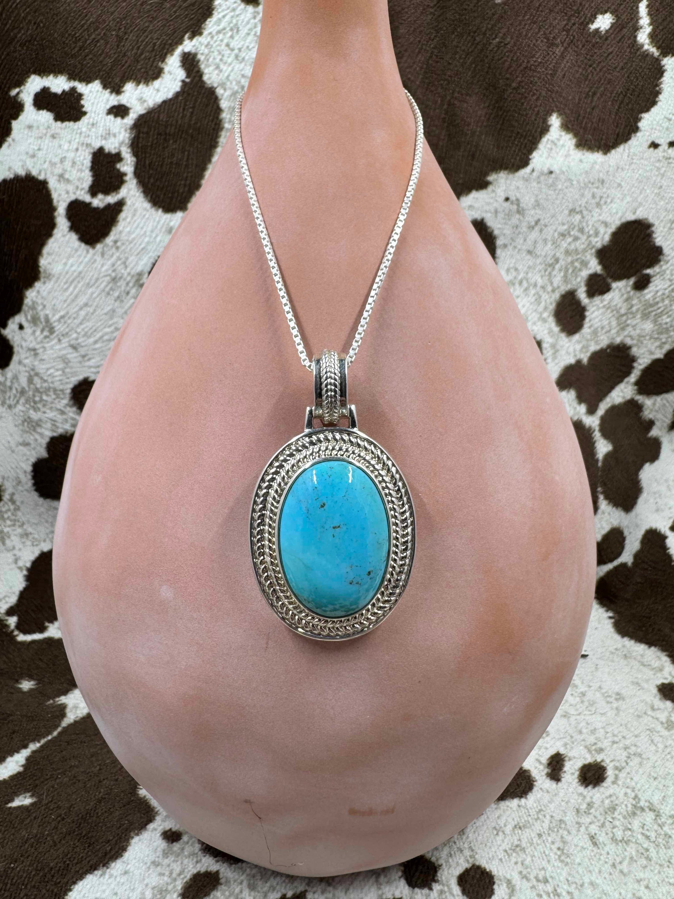 Turquoise Pendant Enhancer hanging on a silver chain on a brown bottle and cowhide background