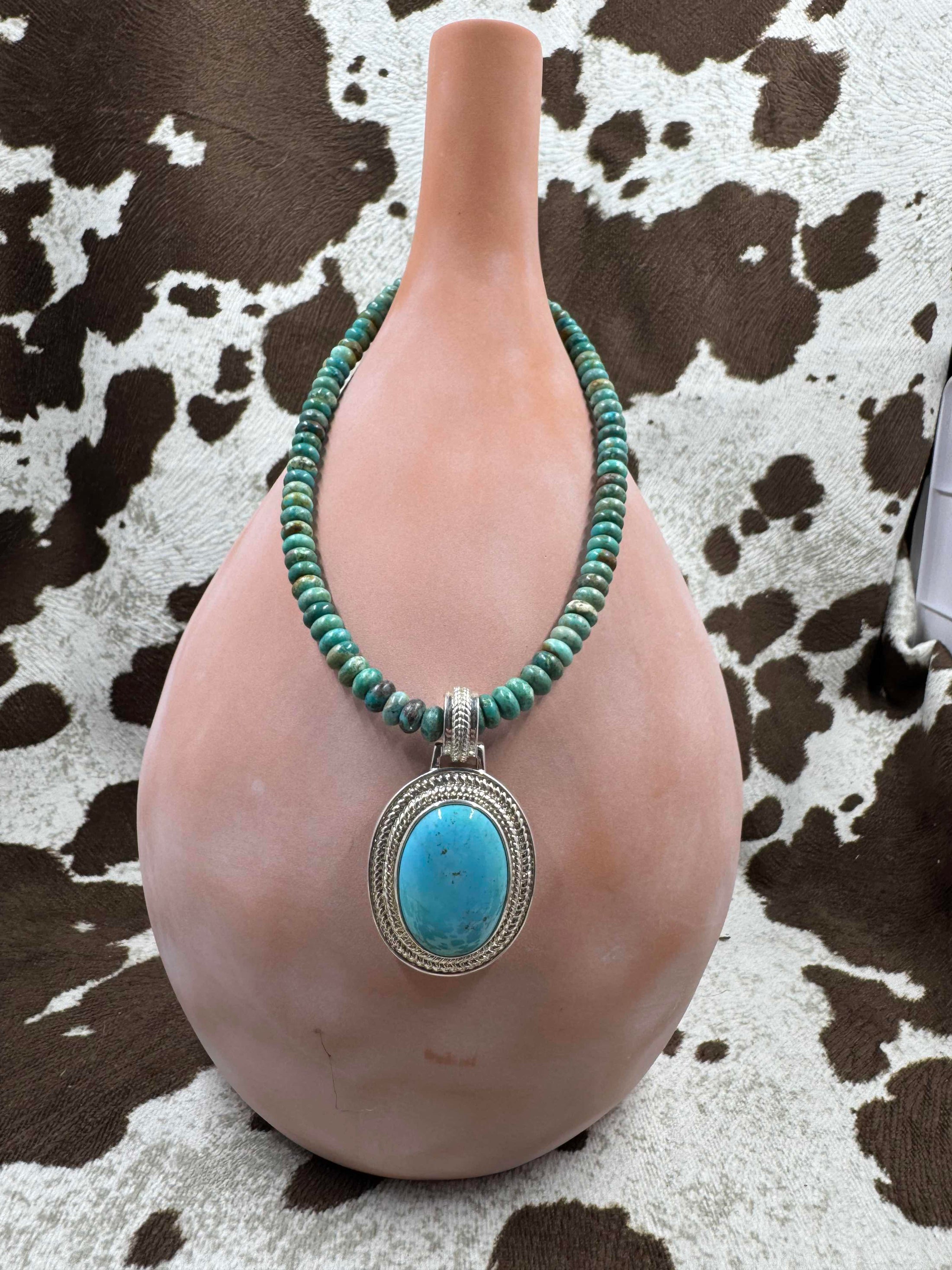 Turquoise Pendant Enhancer hanging on a turquoise chain on brown bottle with cowhide background