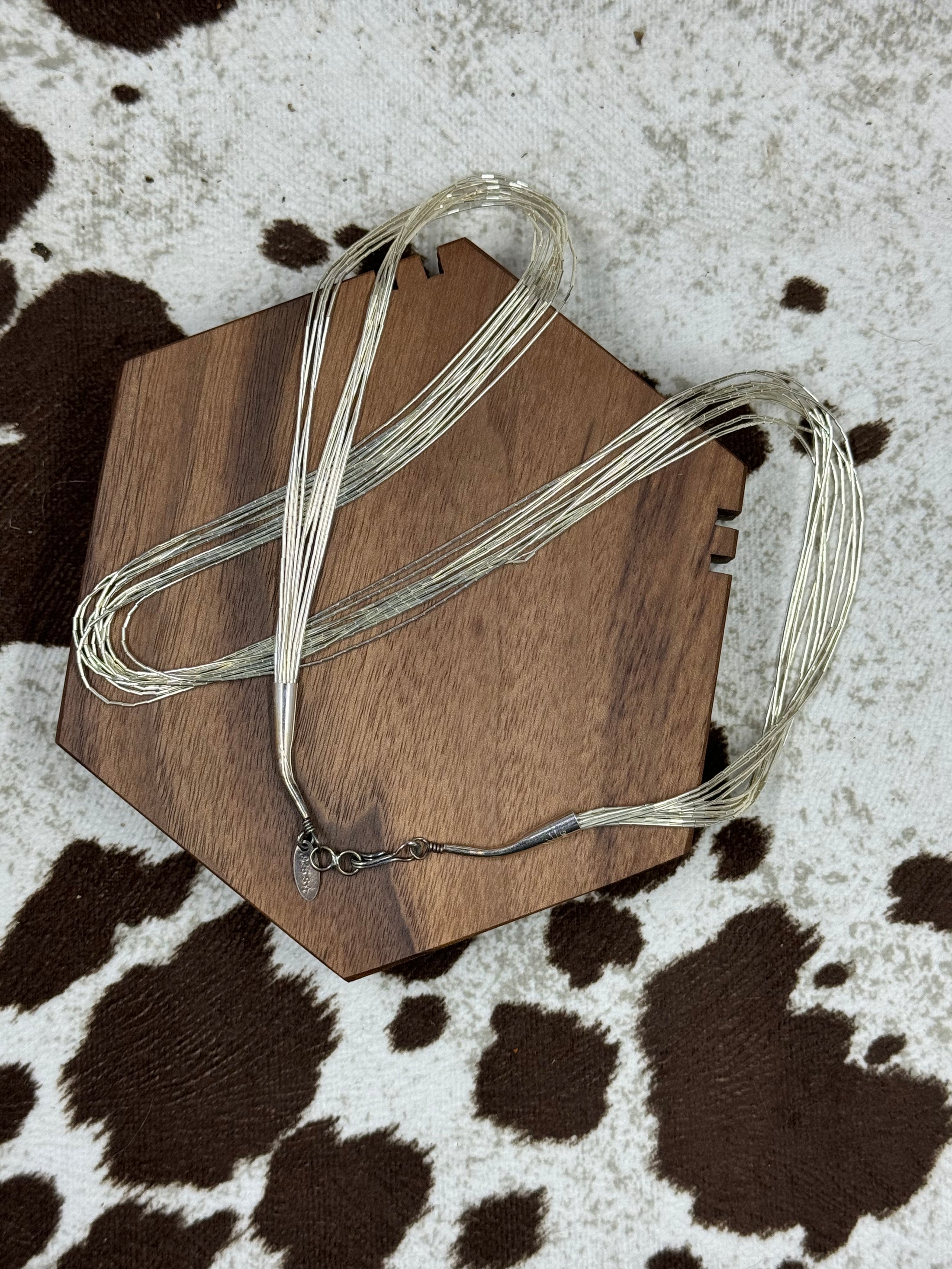 Southwest Style Polished Sterling Silver Liquid 10 strand Necklace laying on wood block with cowhide background