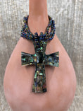 Load image into Gallery viewer, Colorful beaded necklace with inlayed cross on brown bottle 
