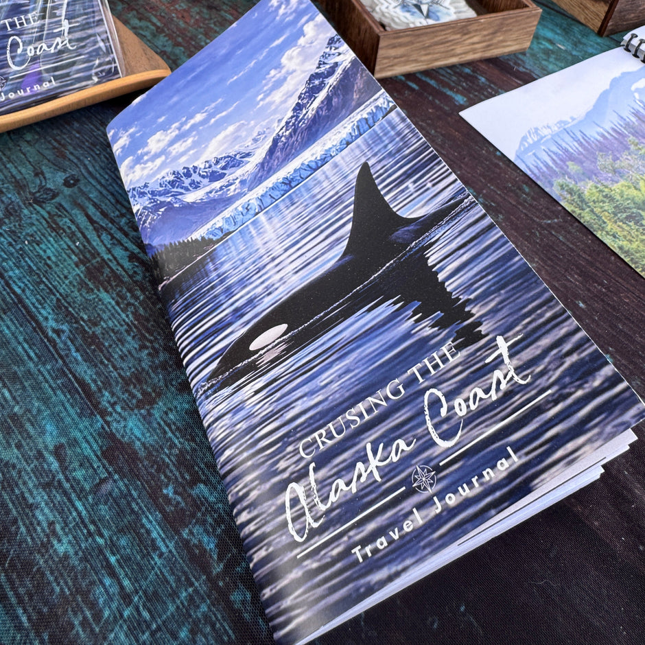 Crusing the Alaska Coast Travel Journal with an orca swimming on it on a table with other items in the background