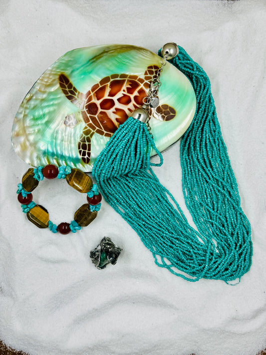 Turquoise colored beaded necklace on turtle jewelry box in the sand with a bracelet and ring