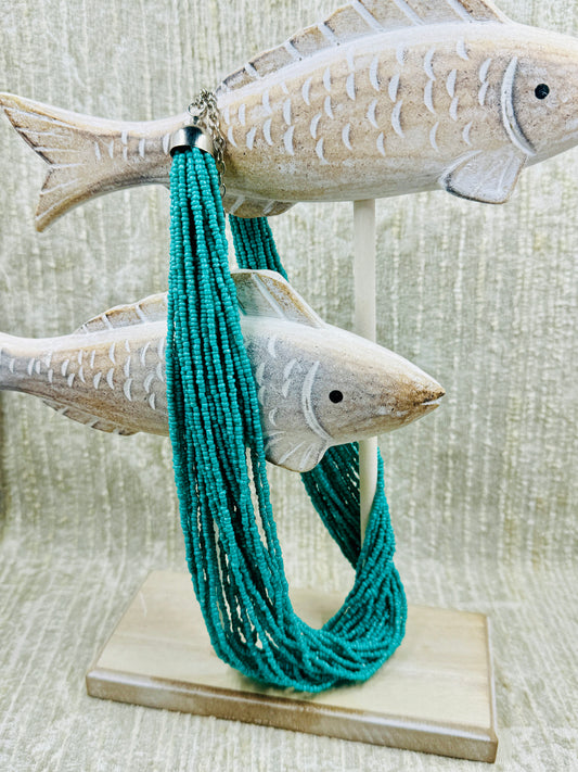 Turquoise colored beaded necklace hanging from fish decoration with cream colored background