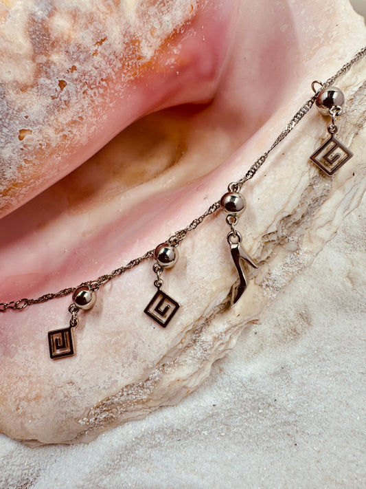 Silver colored ankle bracelet laying on a sea shell in the sand