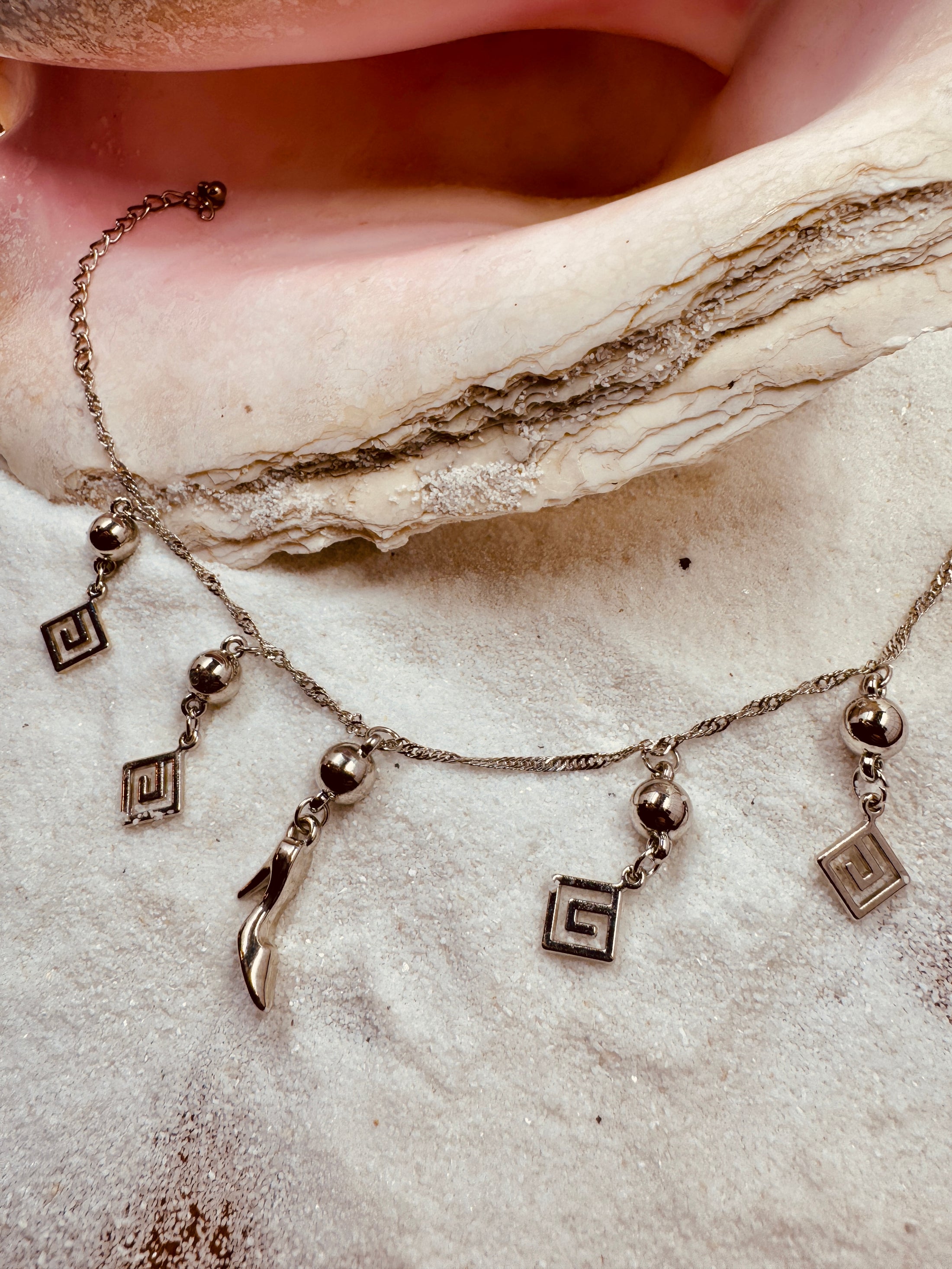 Silver colored ankle bracelet laying on a sea shell in the sand