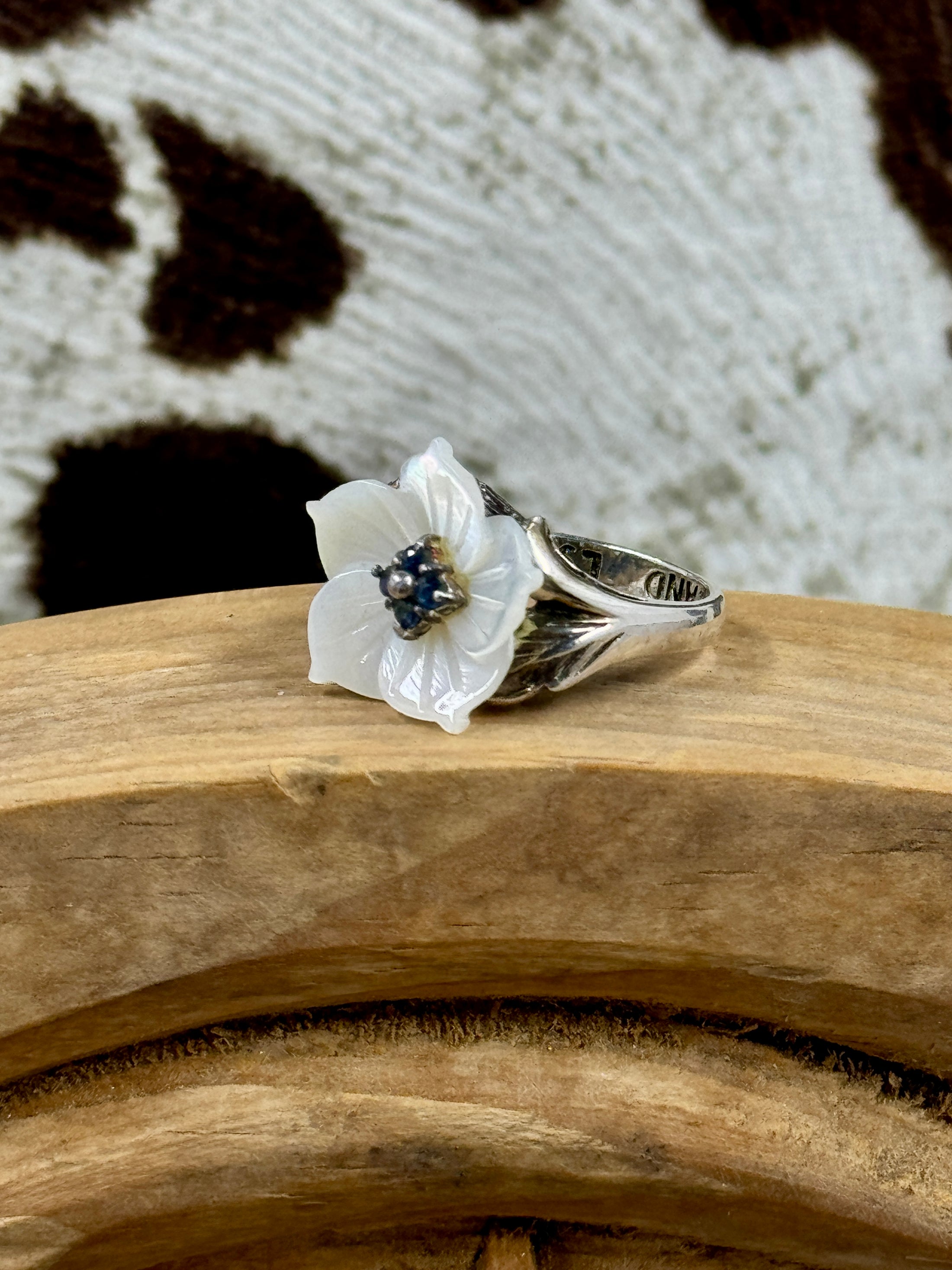 Vintage Mother of Pearl Flower Ring with Sapphire Stones on wood block with cowhide background