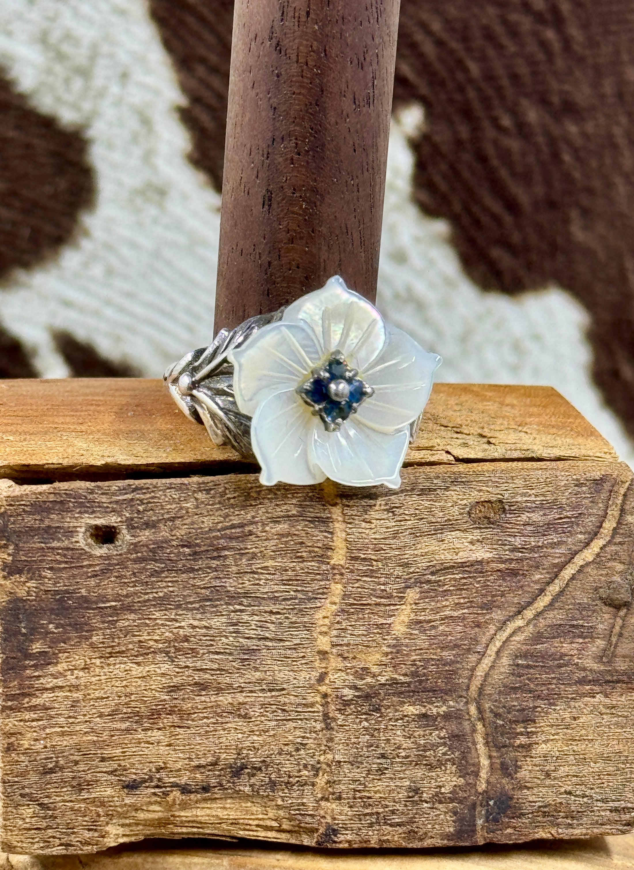 Vintage Mother of Pearl Flower Ring with Sapphire Stones on wood block with cowhide background