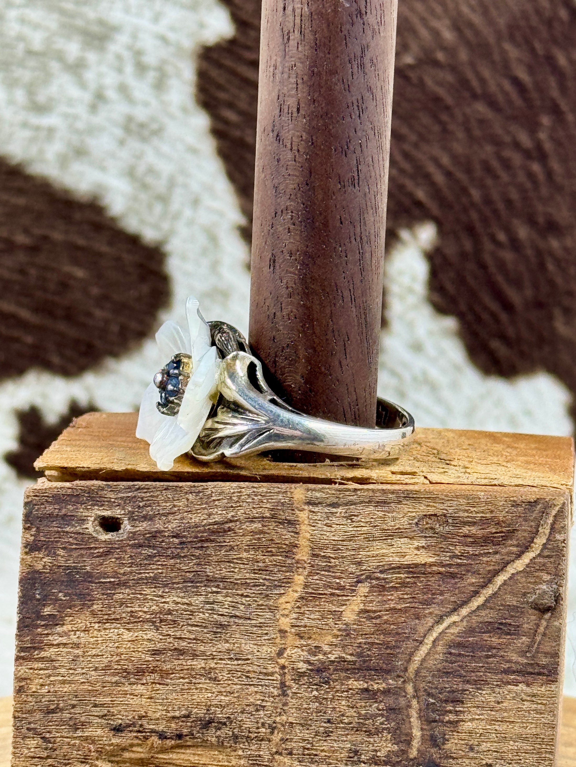 Side view of Vintage Mother of Pearl Flower Ring with Sapphire Stones on wood block with cowhide background