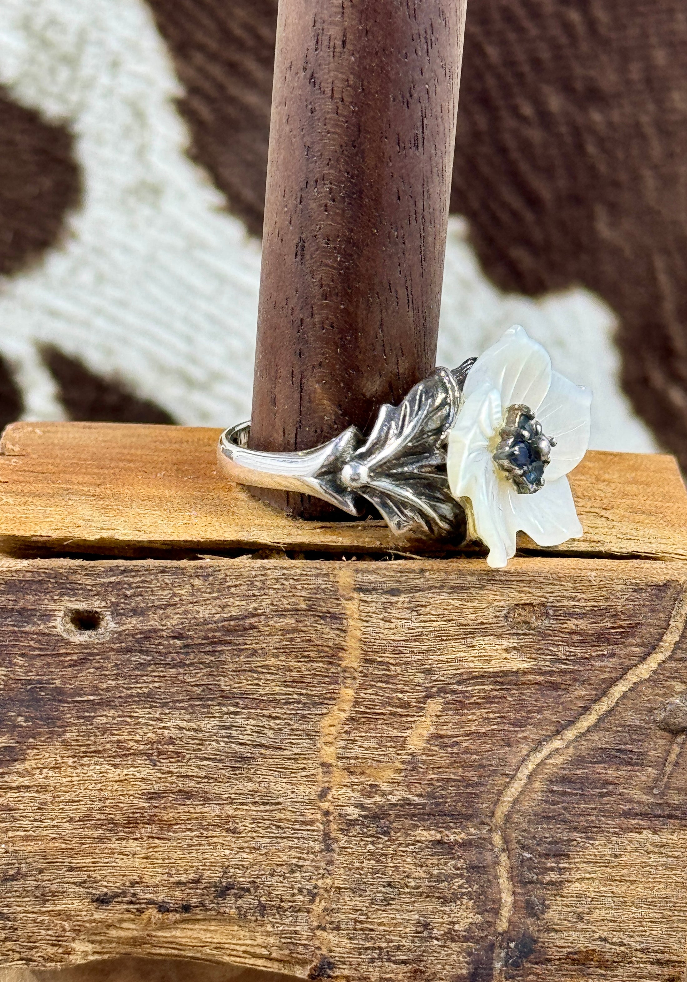 Side view of Vintage Mother of Pearl Flower Ring with Sapphire Stones on wood block with cowhide background