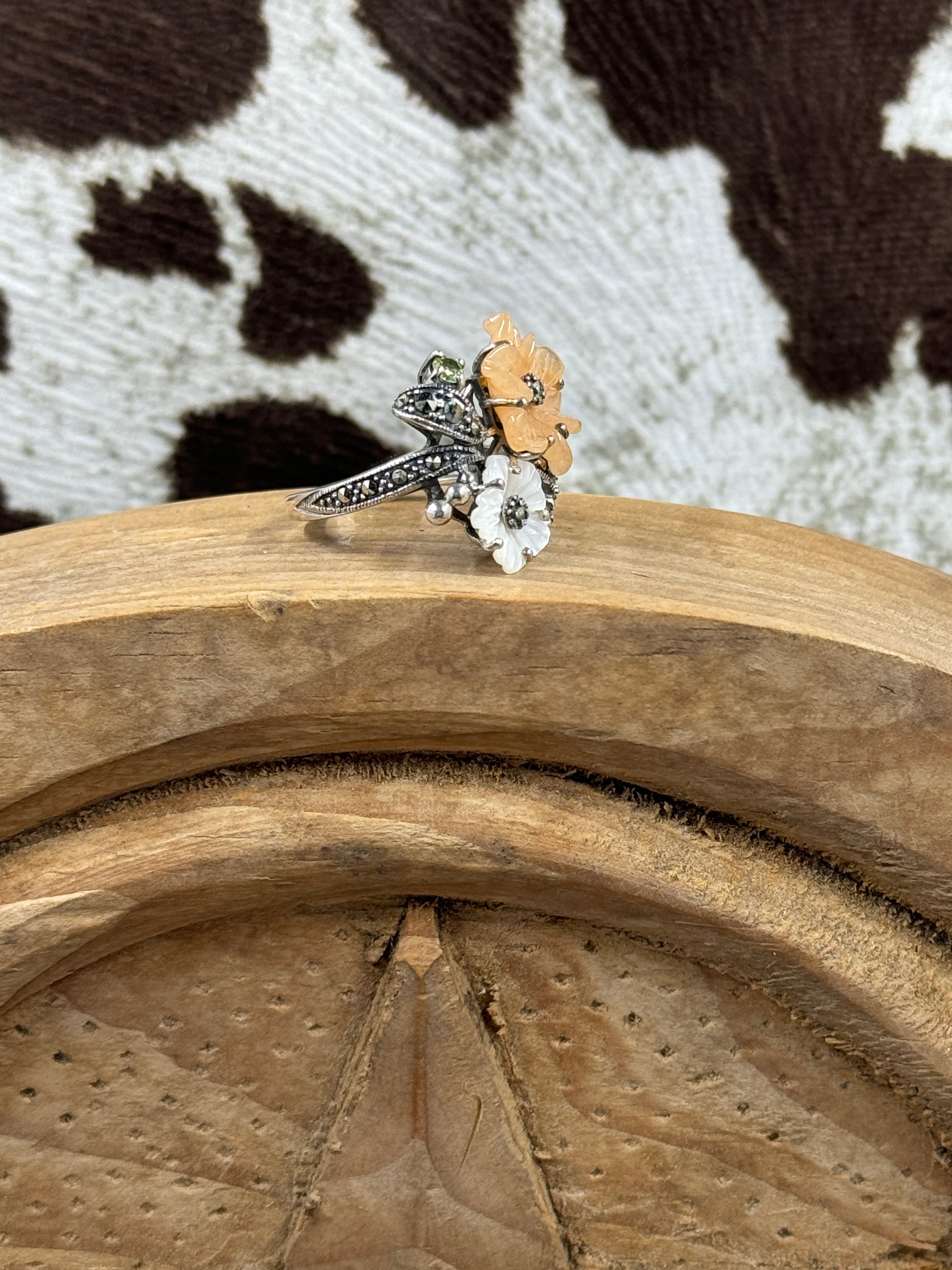 Side view of Jade and Mother of Pearl Flower RIng on wood block with cowhide background