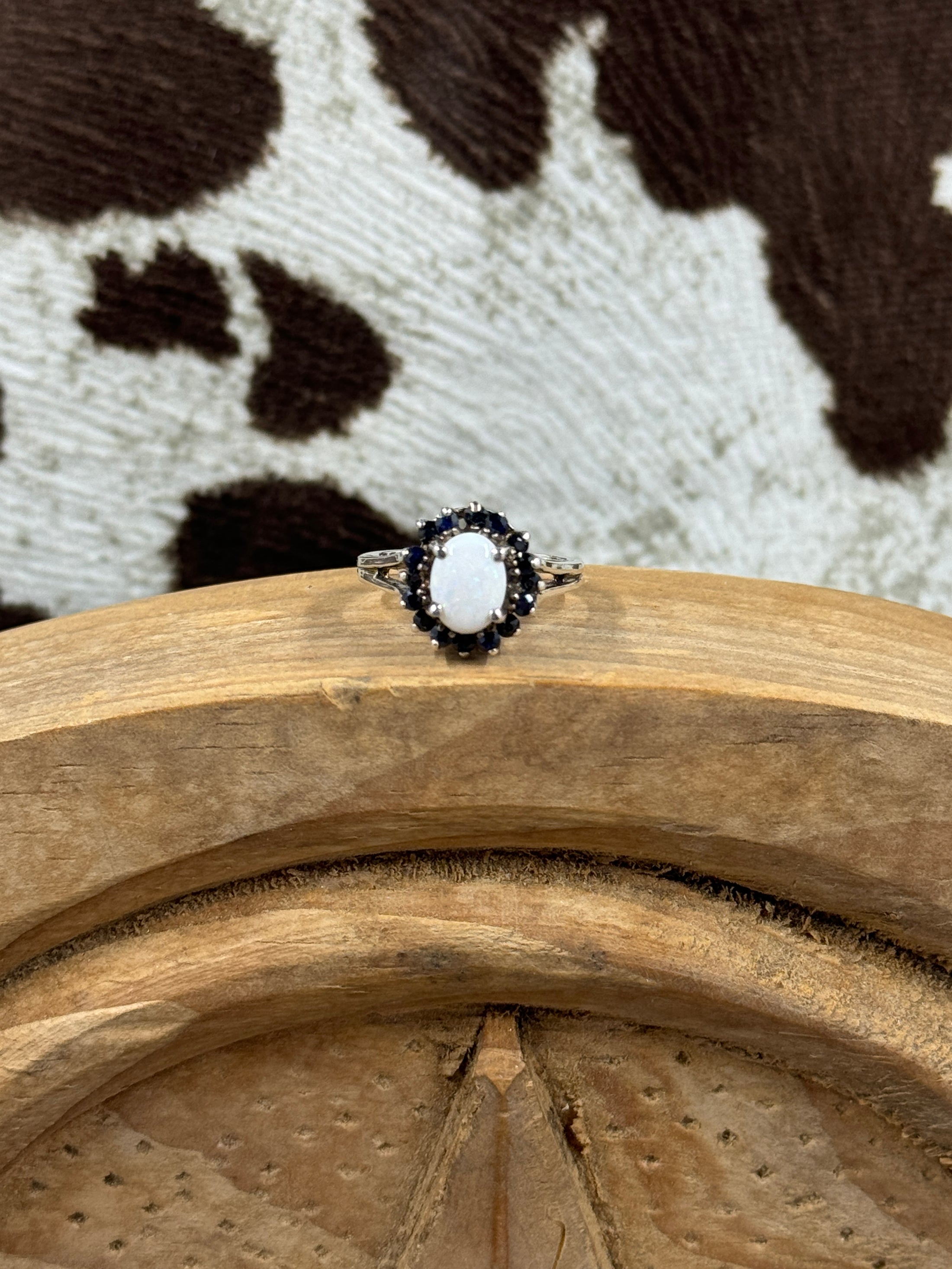 Australian White Opal Halo Sapphire Ring on wood block with cowhide background