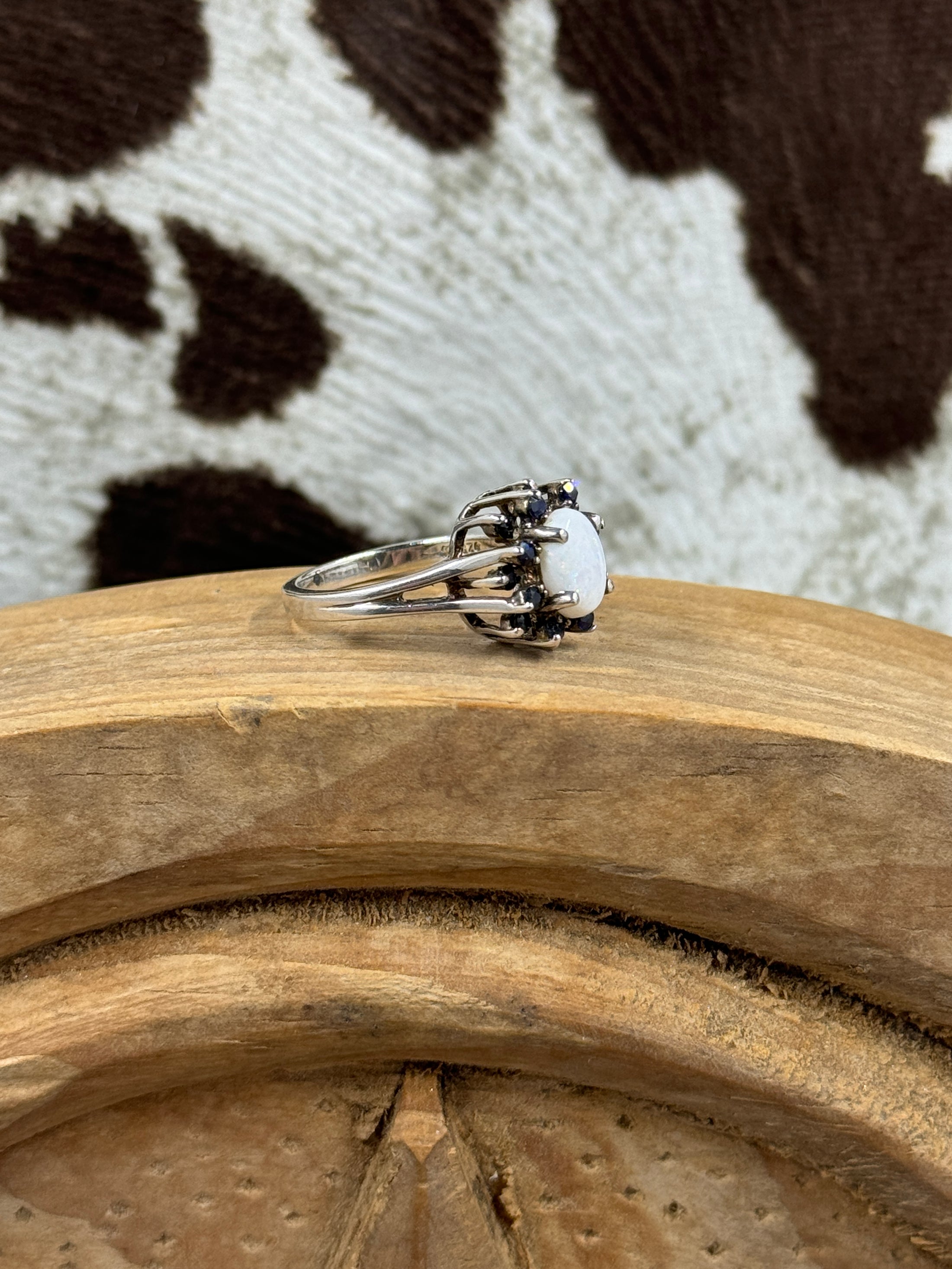 side view of Australian White Opal Halo Sapphire Ring on wood block with cowhide background