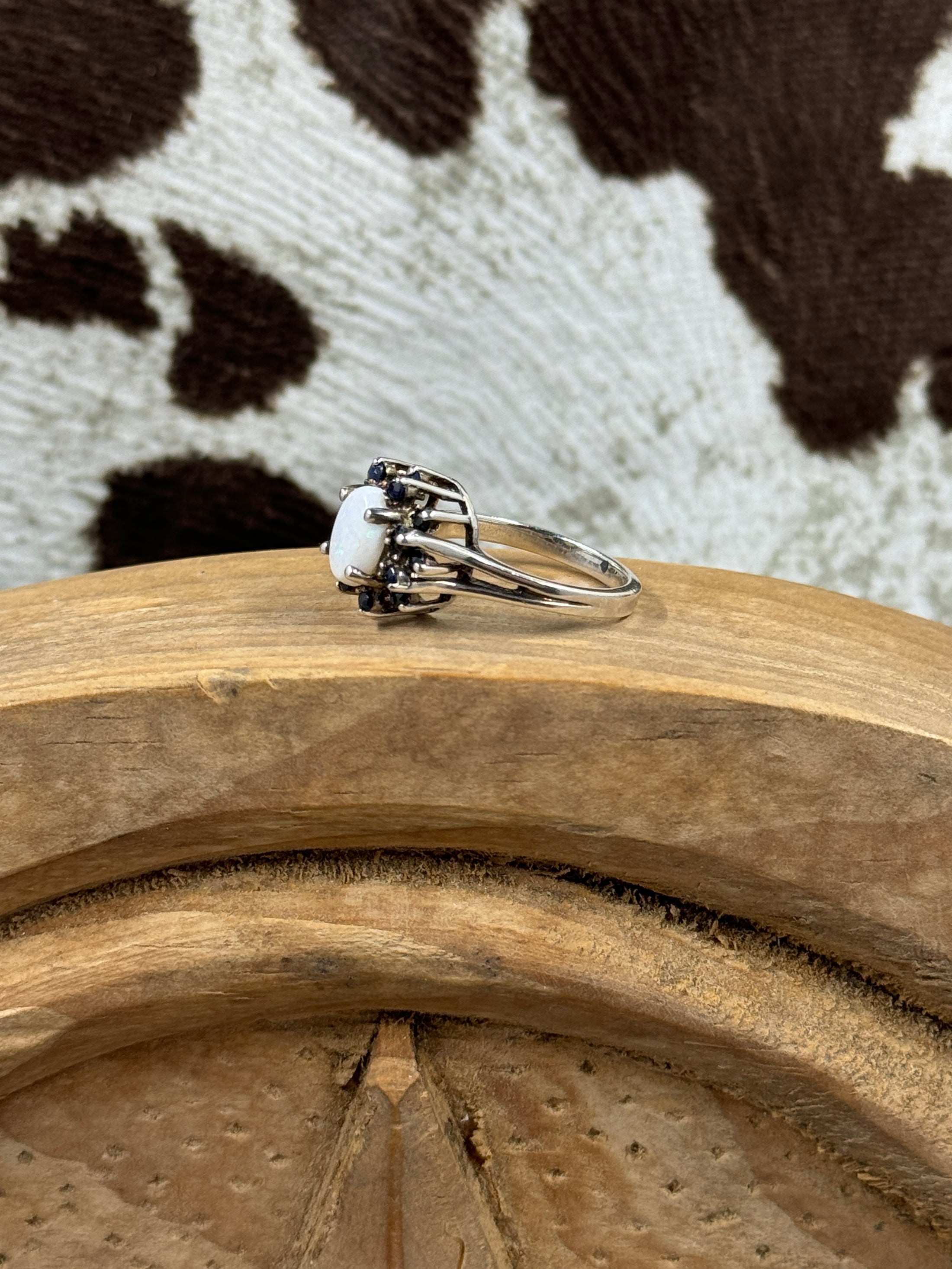 side view of Australian White Opal Halo Sapphire Ring on wood block with cowhide background