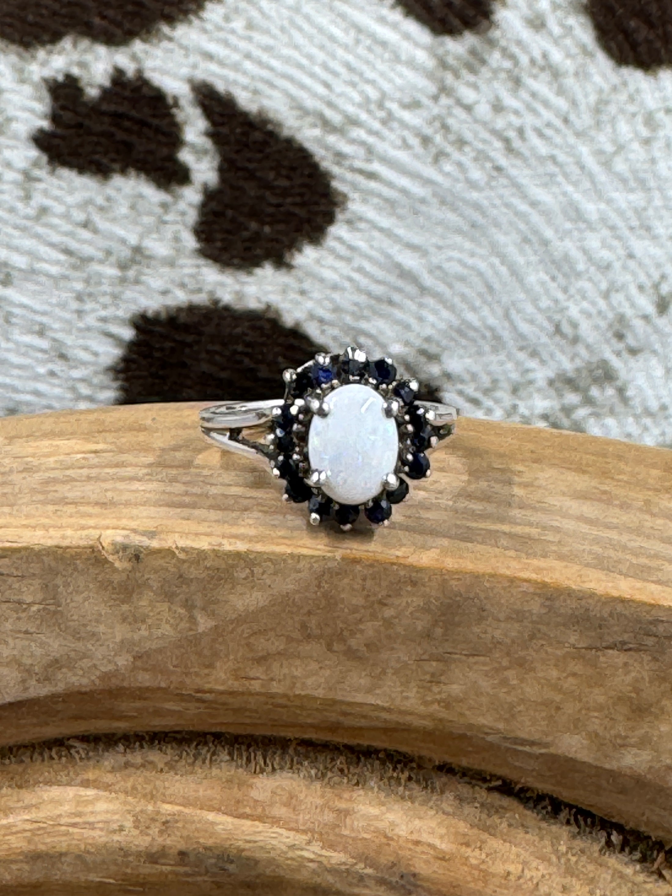 Australian White Opal Halo Sapphire Ring on wood block with cowhide background