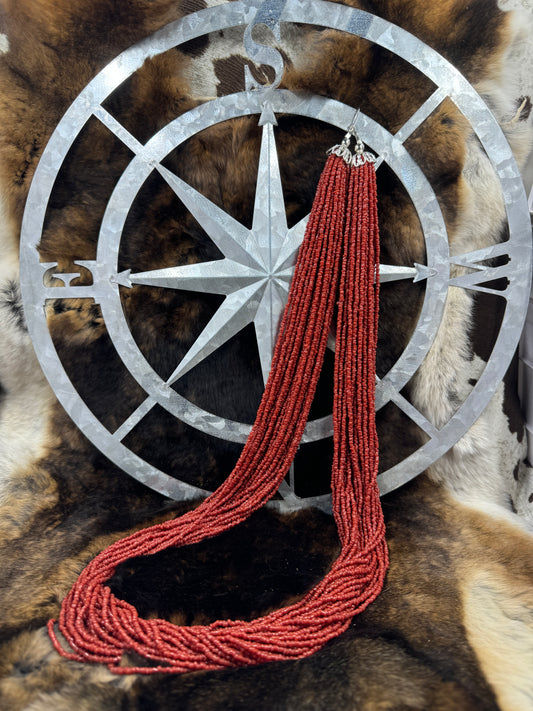 Lee Sands Red Seed Bead Multi Strand hanging from compass sign with fur background