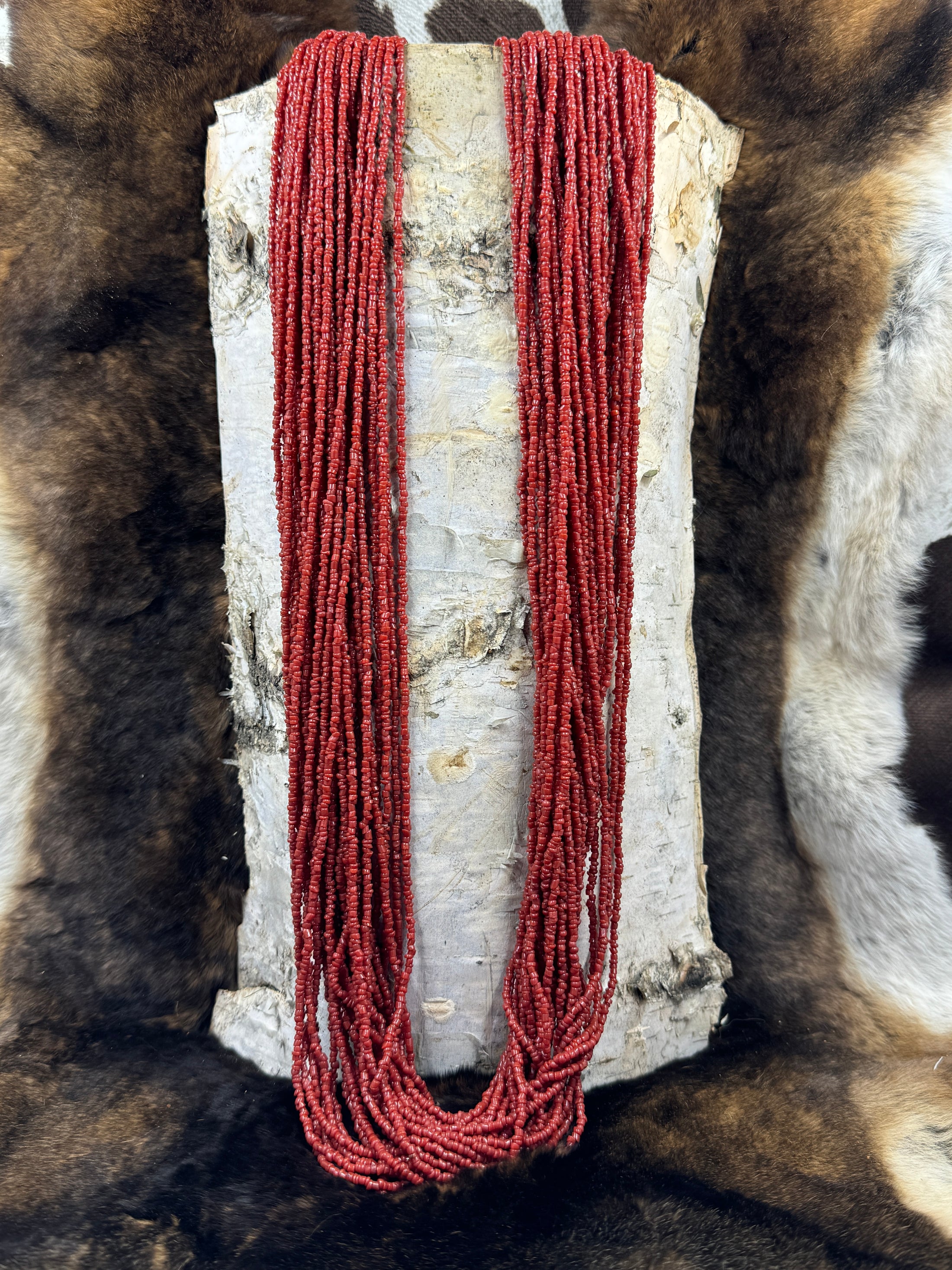 Lee Sands Red Seed Bead Multi Strand hanging over a piece of birch bark and a fur background