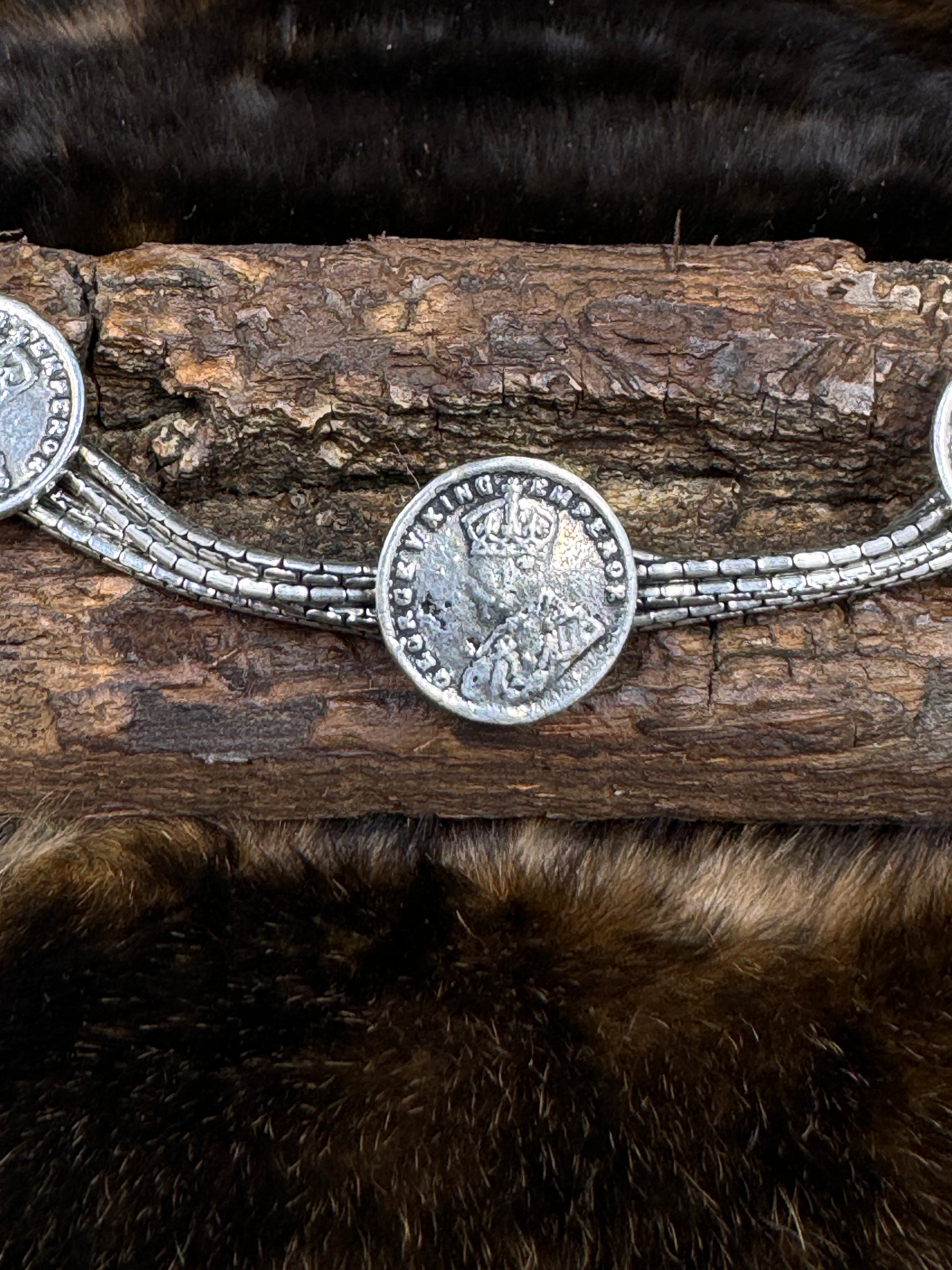 Chain Bracelet with Coins of George V on wood block with dark fur background