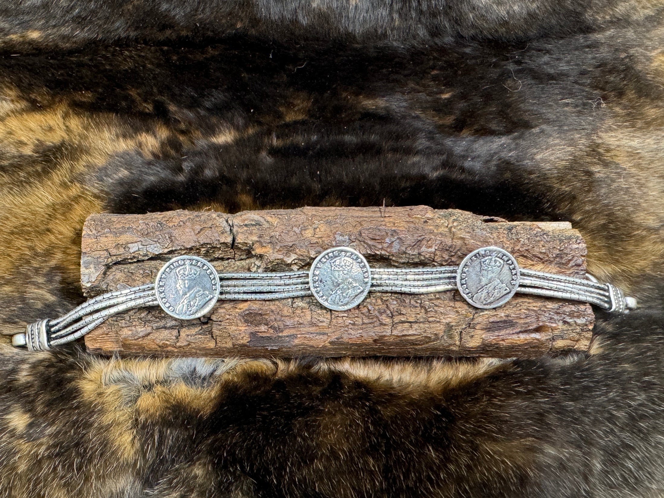 Chain Bracelet with Coins of George V on wood block with dark fur background