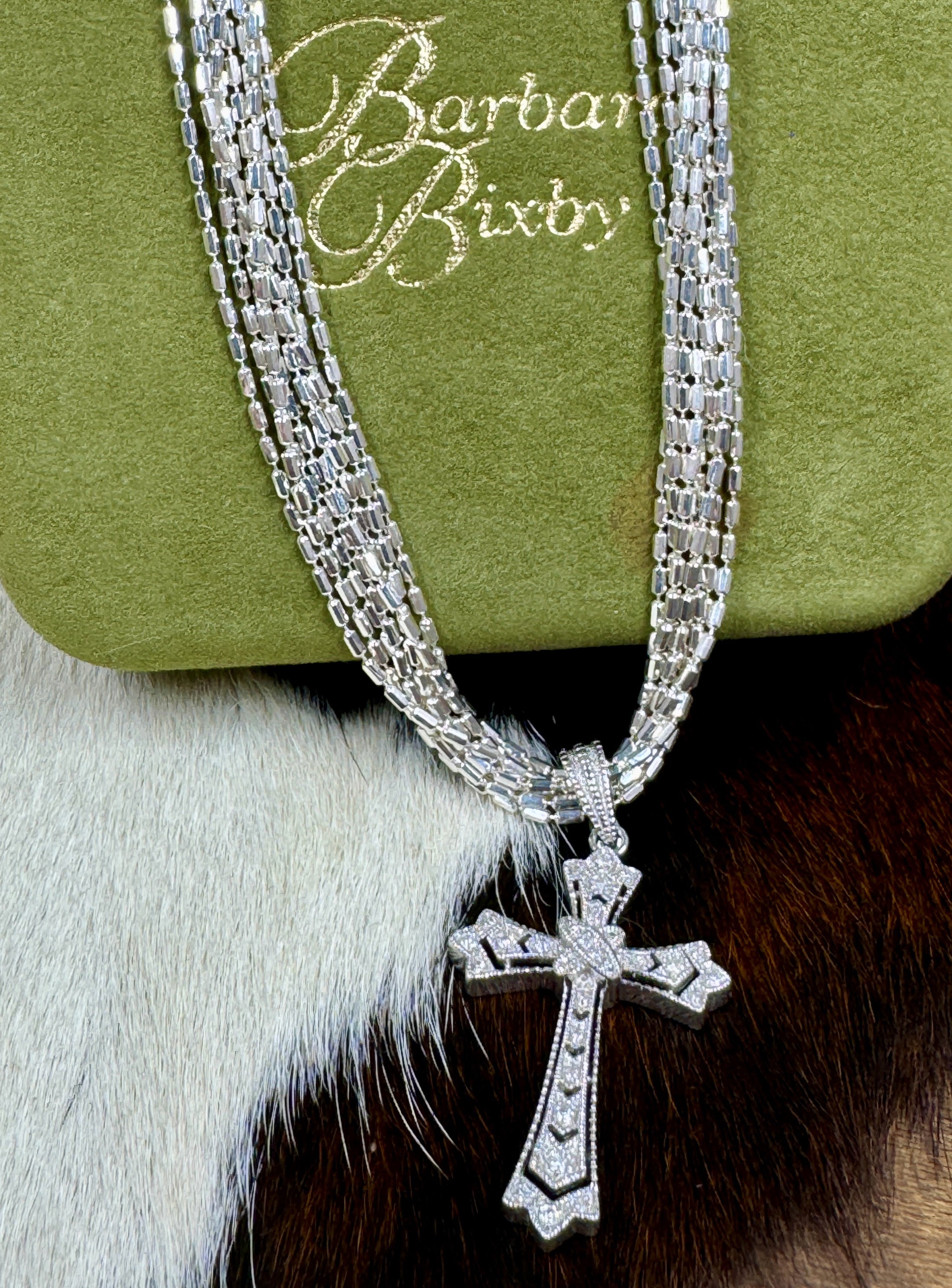 Diamond Chip and Sterling Silver Cross Pendant by Barbara Bixbie with Silver Chain on cowhide background and with green box that says Barbara Bixby