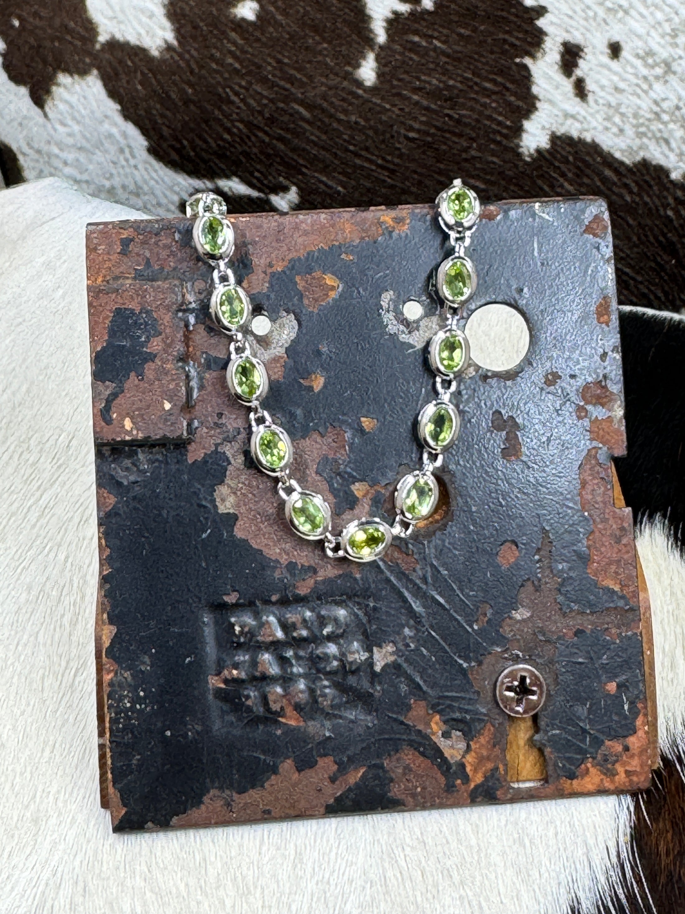 Silver Stainless Steel and Peridot Gem Bracelet on metal stand with cowhide background