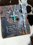 Load image into Gallery viewer, D'joy Emerald Cross Necklace and Bracelet Set in Sterling on black metal stand with cowhide background
