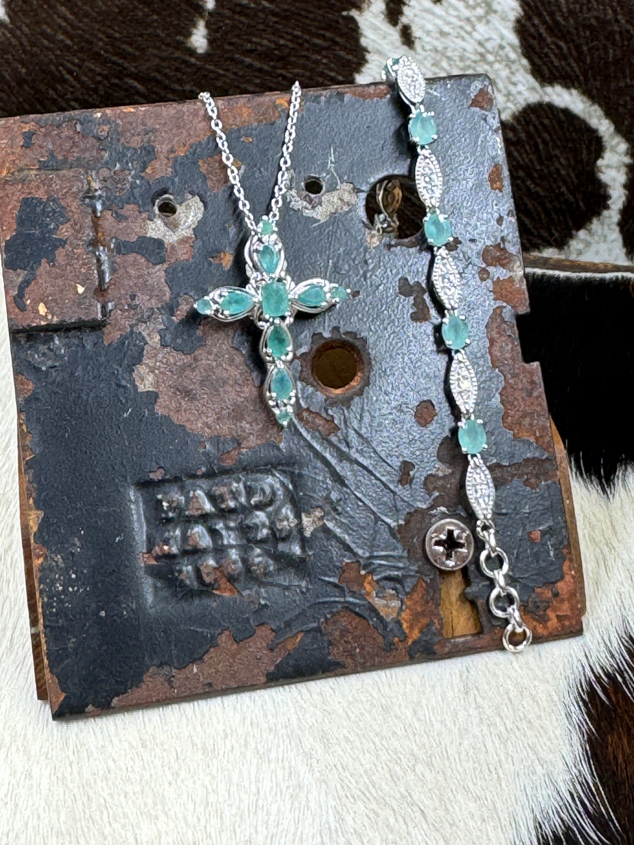 D'joy Emerald Cross Necklace and Bracelet Set in Sterling on black metal stand with cowhide background