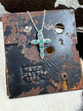 Load image into Gallery viewer, D'joy Emerald Cross Necklace set in sterling on black metal stand with cowhide background
