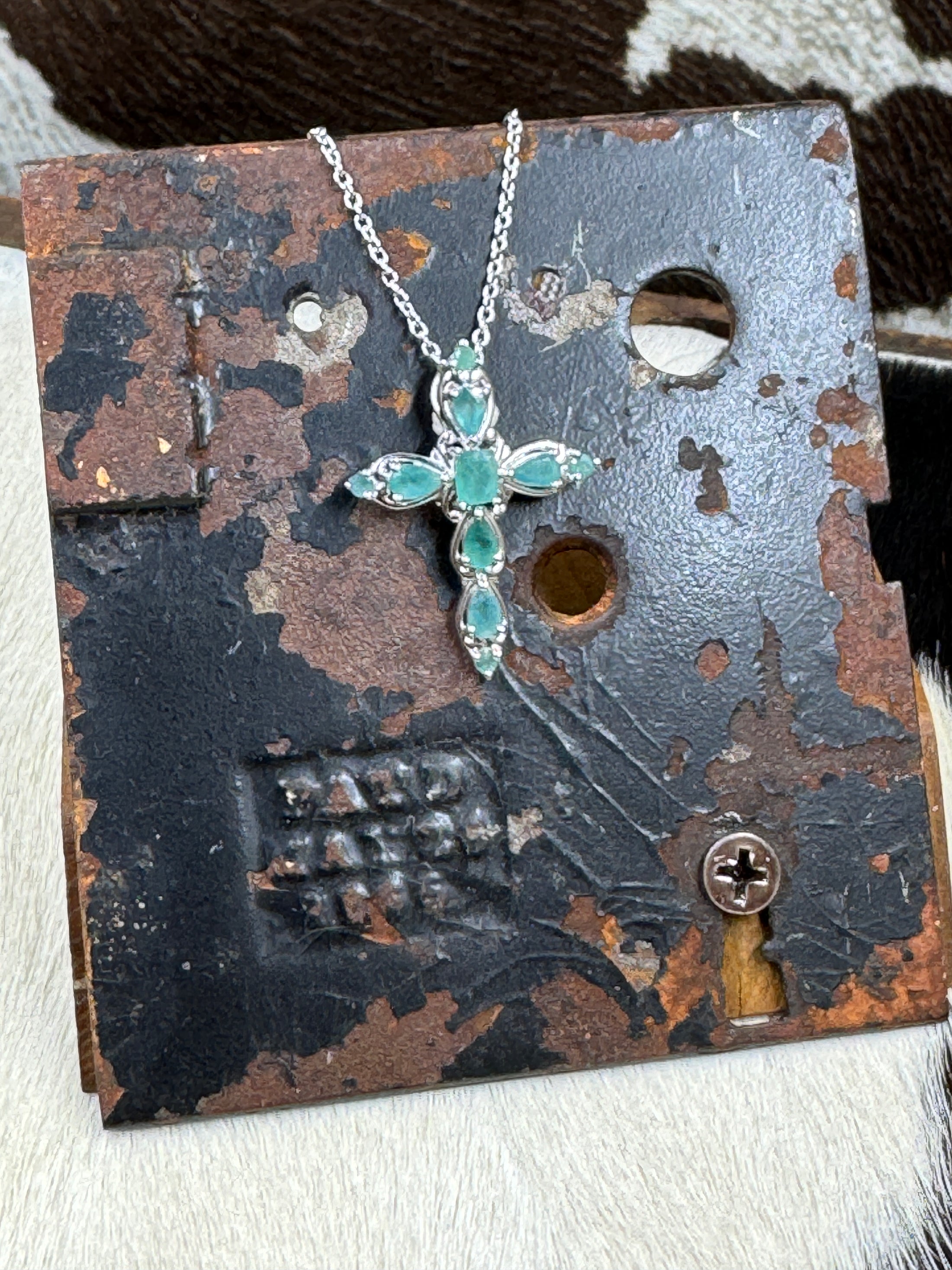 D'joy Emerald Cross Necklace set in sterling on black metal stand with cowhide background