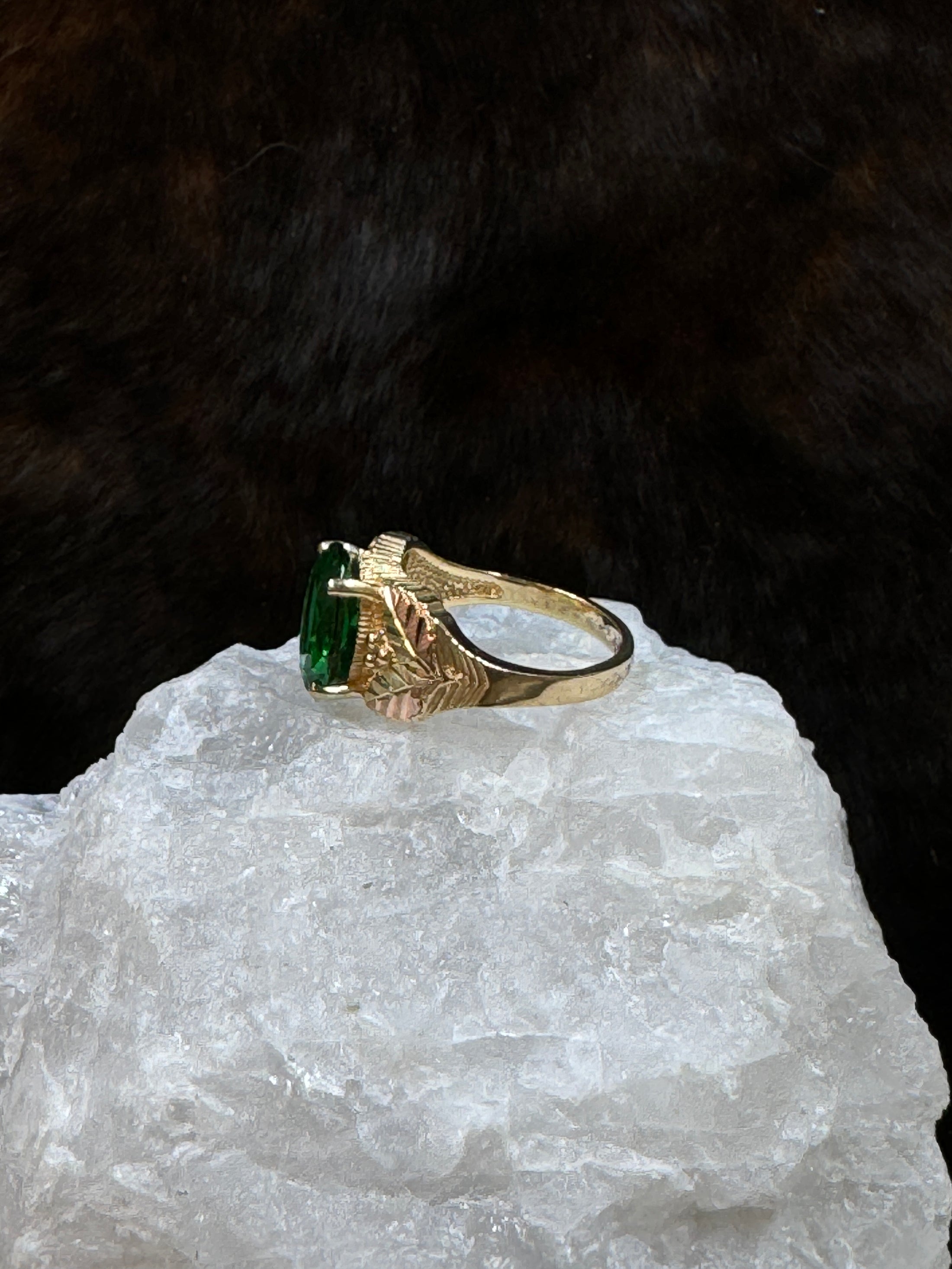 Side view of Black Hills Gold Coleman 10K Lab Created Emerald  on white rock with fur background