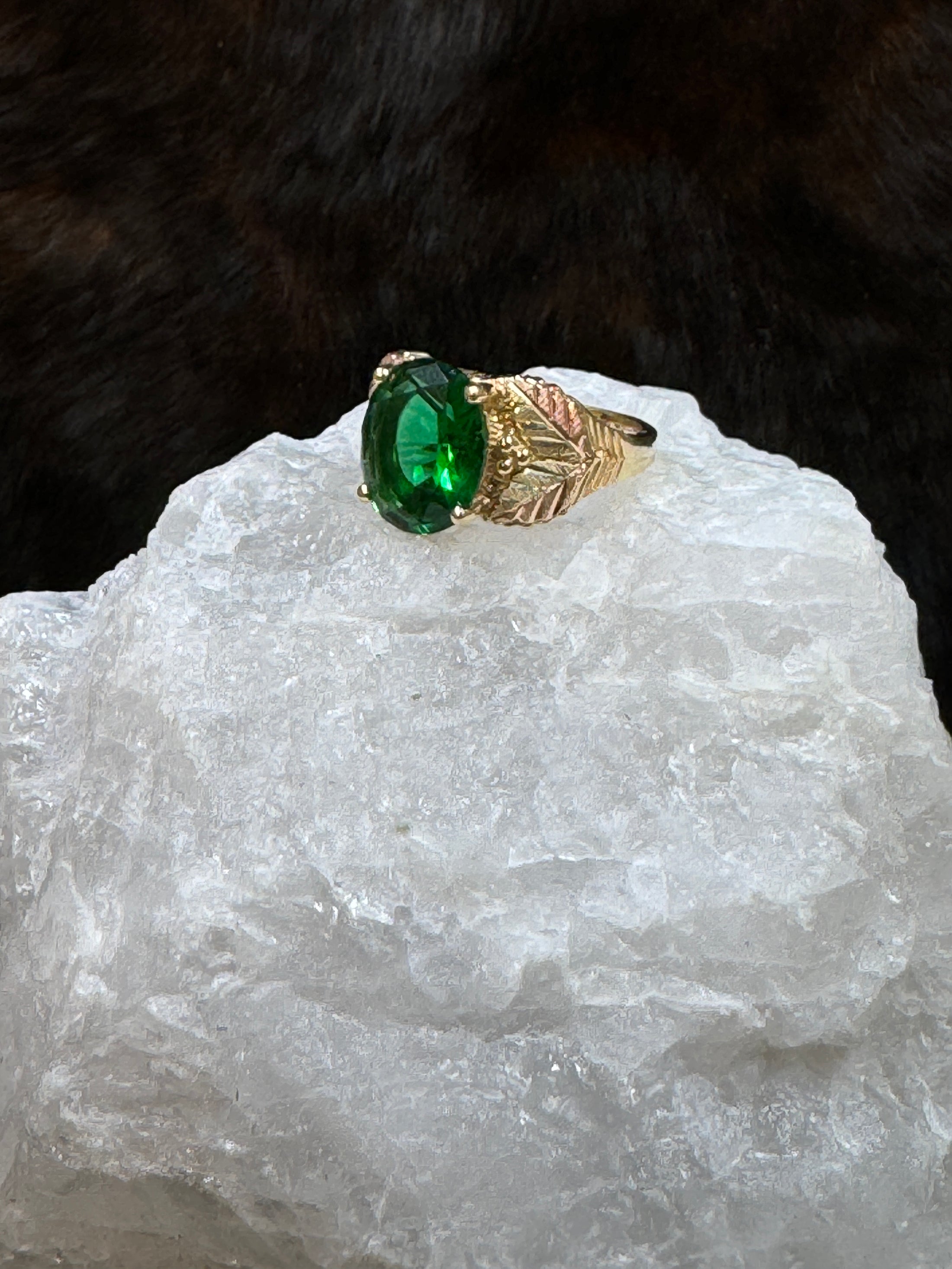 Side view Black Hills Gold Coleman 10K Lab Created Emerald  on white rock with fur background