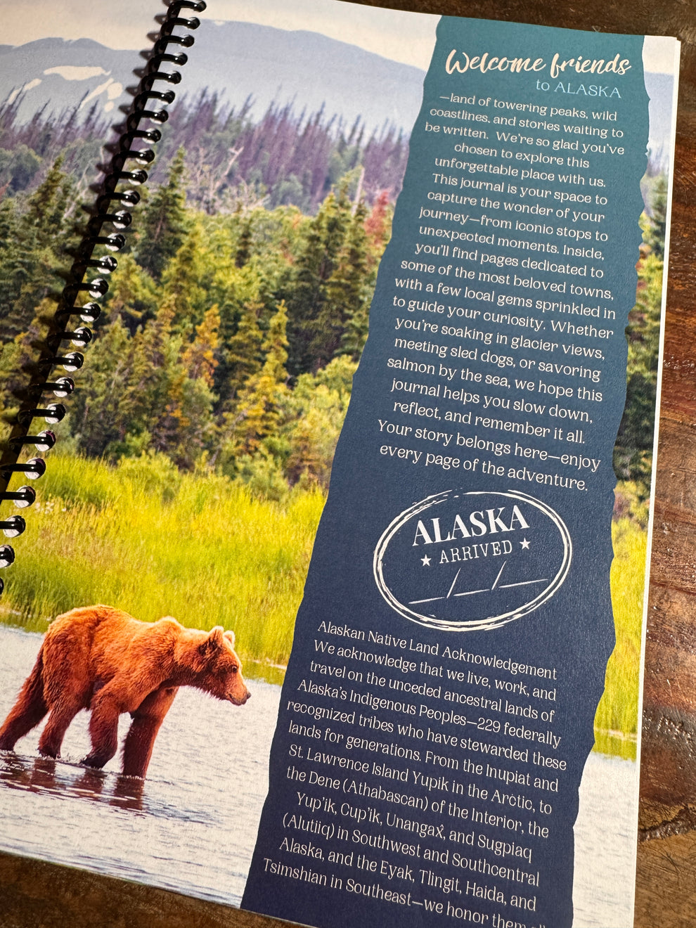 A spiral-bound notebook page featuring a scenic Alaska landscape with a brown bear in the foreground and a large text column headed 'Welcome friends' and 'Alaska Archives.'.