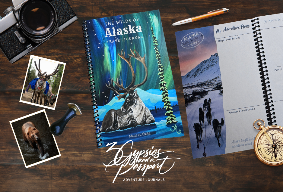Alaska travel journal with reindeer illustration on a wooden surface with photos and accessories.